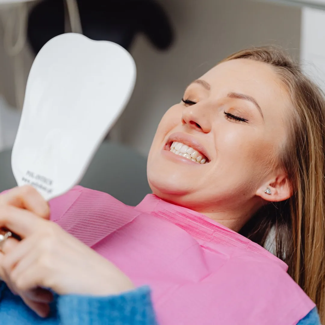 Woman admiring her brightened, whitened smile in a hand mirror at the dentist